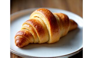 Sekeping croissant keemasan yang baru dibakar di atas pinggan.